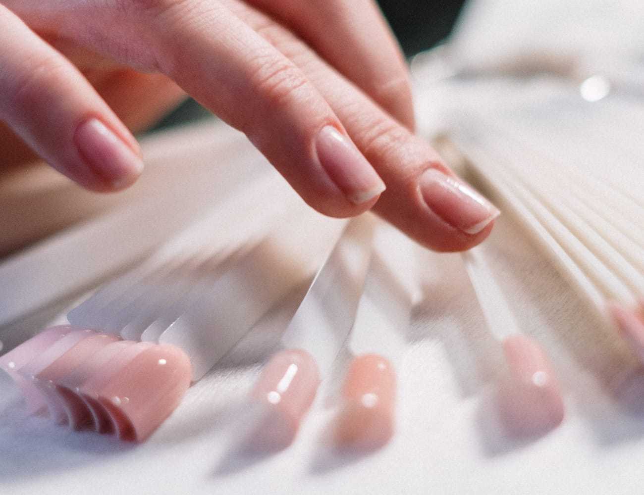 Hand reaches for nail color samples on display board.